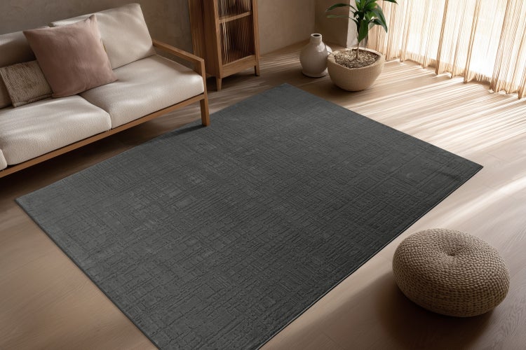 Ein rechteckiger Teppich mit strukturierter Oberfläche in einem Wohnraum mit hellen Holzmöbeln, einem Sofa und einer Zimmerpflanze.