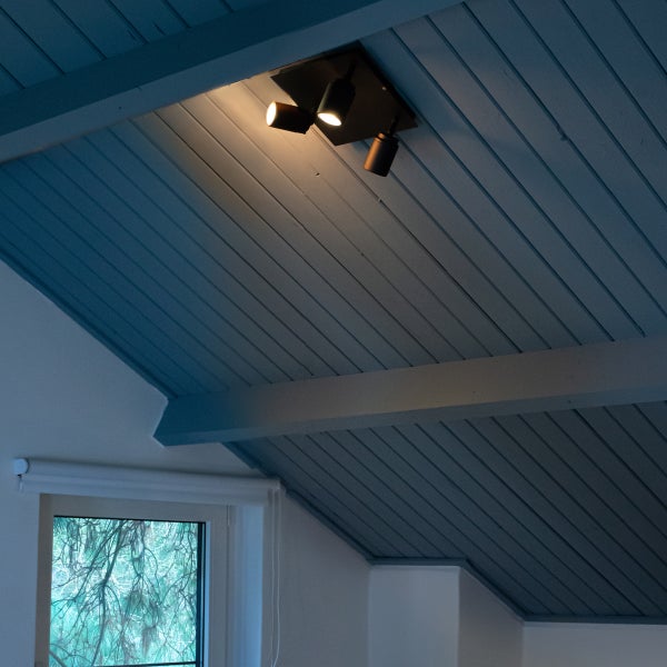 Deckenleuchte mit drei Strahlern an einer Holzdecke in einem Dachgeschosszimmer.
