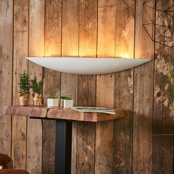 Bogenförmige Wandleuchte in Weiß an einer rustikalen Holzwand über einem Massivholztisch mit indirekter, warmweißer Beleuchtung.