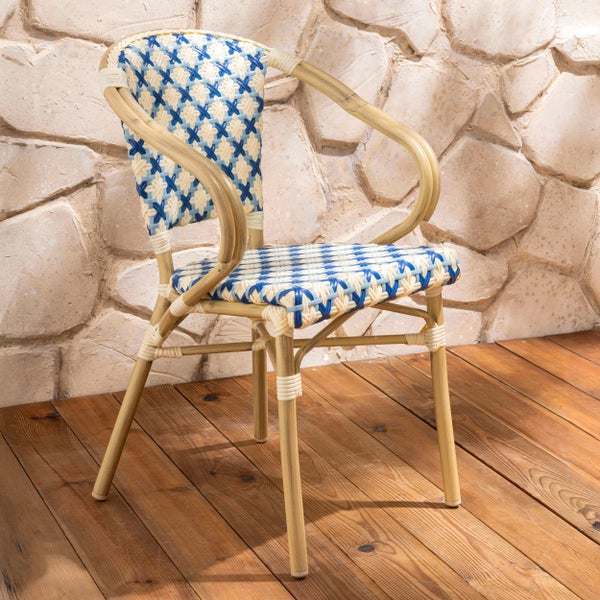 Bistro-Armlehnstuhl mit blau-weißem Geflecht und Gestell in Rattan-Optik auf einem Holzboden vor einer Steinwand.