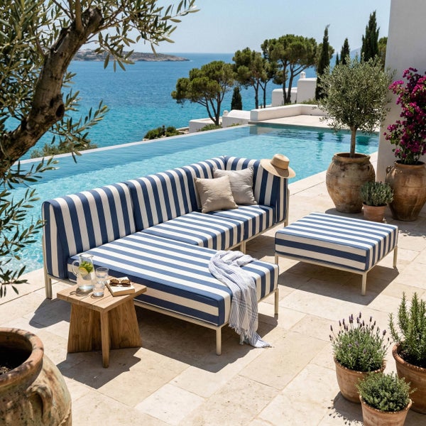 Mediterrane Terrasse mit blau-weiß gestreiftem Loungesofa, Hocker, Holzbeistelltisch und Pflanzen neben einem Pool mit Meerblick.
