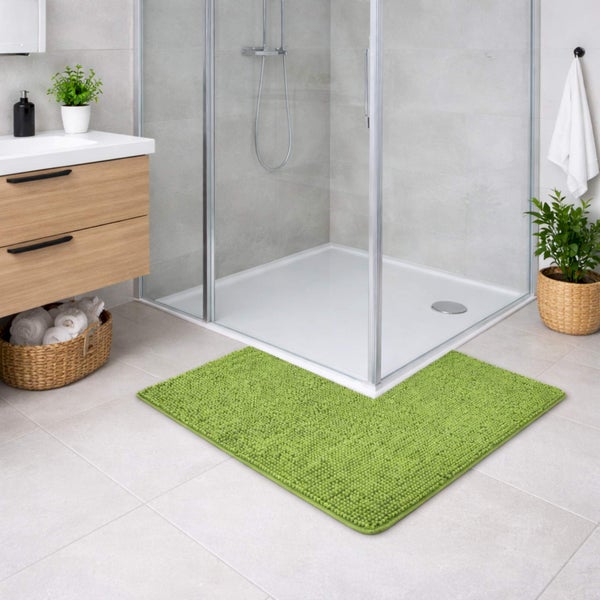 Helles, modern gestaltetes Badezimmer mit einer grünen, weichen Badematte mit Eckausschnitt vor einer gläsernen Duschkabine.