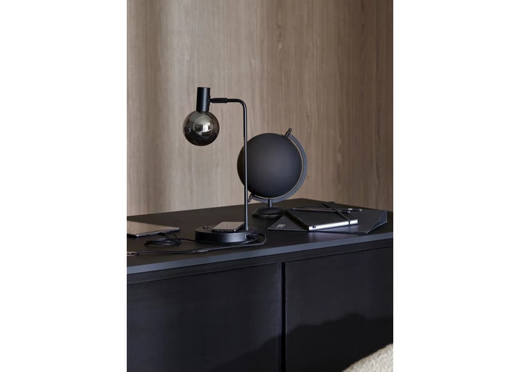 Moderne Schreibtischleuchte mit kugelförmigem Glaskopf, Wireless Charging Station und USB Anschluss auf einem dunklen Schreibtisch.