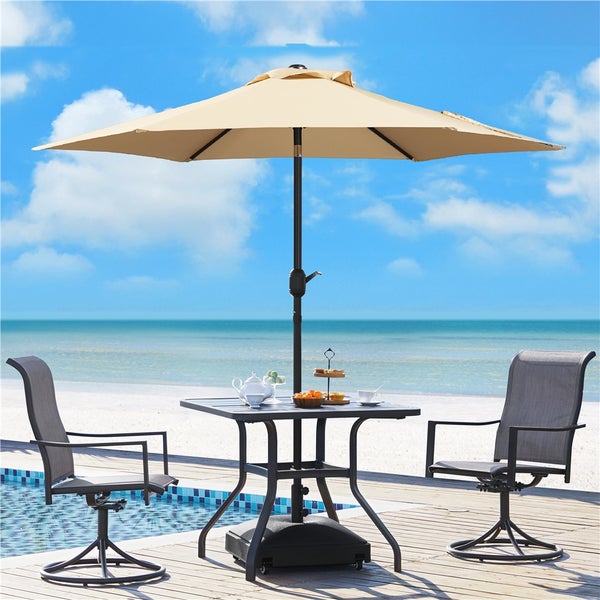 Gartenmöbel-Set mit beigem Sonnenschirm, quadratischem Metalltisch und zwei grauen Mesh-Drehstühlen auf einer Terrasse am Strand.