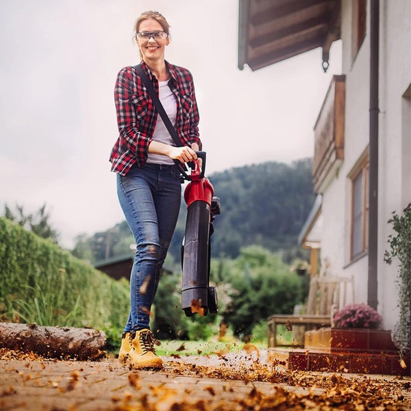 Eine Frau verwendet einen Laubbläser auf einer gepflasterten Auffahrt vor einem Haus, um trockenes Laub zu entfernen.
