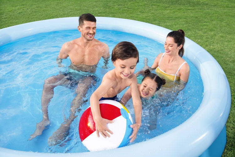 Familie mit zwei Kindern spielt mit einem Wasserball in einem runden aufblasbaren Pool auf einer Rasenfläche.