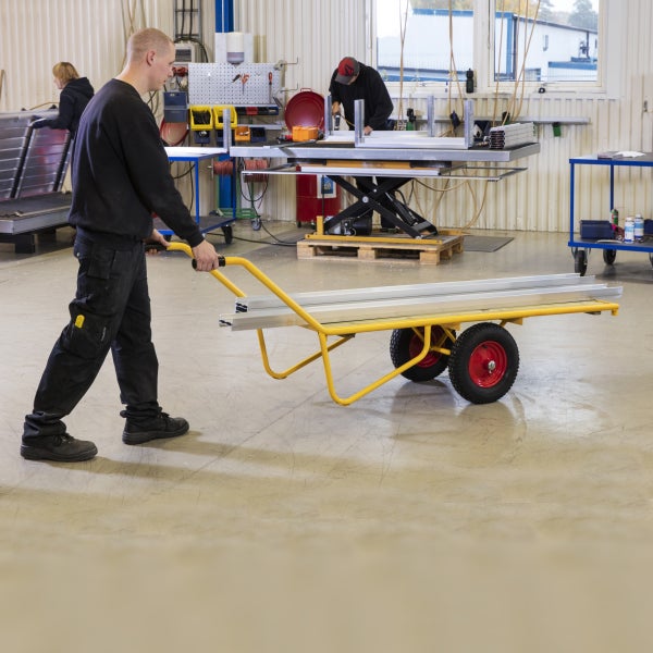 Mann schiebt Bollerwagen mit Aluminiumprofilen in Werkstatt