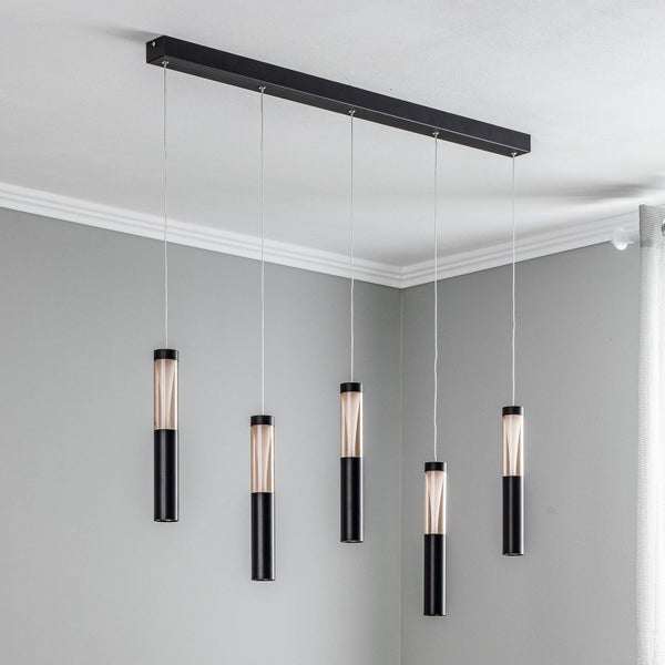 Schwarze Pendelleuchte mit fünf zylindrischen Glasschirmen an einer rechteckigen Deckenhalterung in einem hellen, modernen Raum.