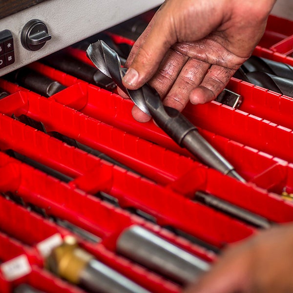Eine Hand hält einen Bohrer über einer roten Werkzeugkiste