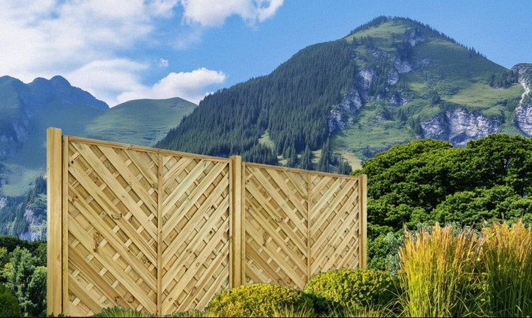 Holzzaun mit Rautenmuster im Garten vor Bergkulisse.