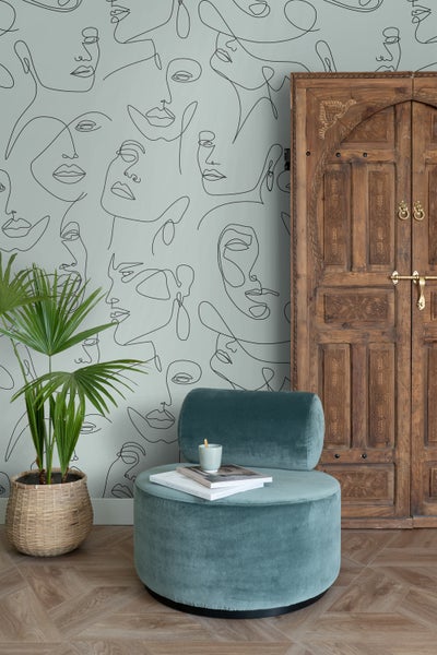 Wohnraum mit Zimmerpflanze, Polsterhocker, Holztür und Tapete mit Gesichtermuster