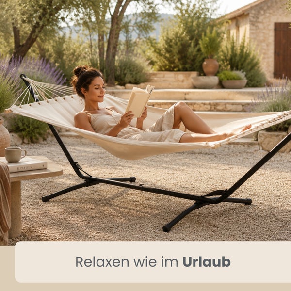 Stabhängematte mit Metallgestell in einem hellen Garten, eine Frau liegt entspannt in der Hängematte und liest ein Buch.