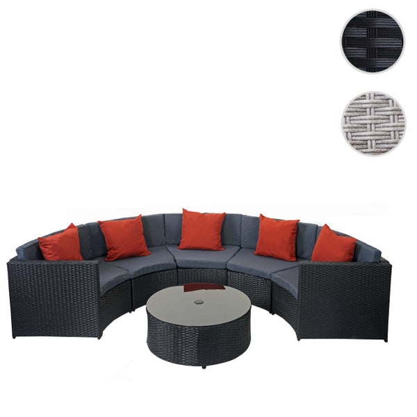 Gebogene Garten-Lounge aus Polyrattan mit rundem Glastisch, grauen Sitzauflagen und roten Zierkissen.