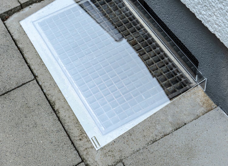 Kellerfensterabdeckung aus Kunststoff auf einem Betonschachtgitter