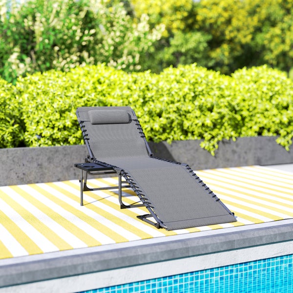 Verstellbare Gartenliege mit Kopfpolster und seitlicher Ablage am Pool auf einem gestreiften Teppich vor grünen Hecken.