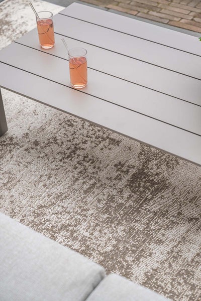 Gemusterter Outdoor-Teppich unter einem grauen Gartentisch aus Lamellen auf einer Terrasse.