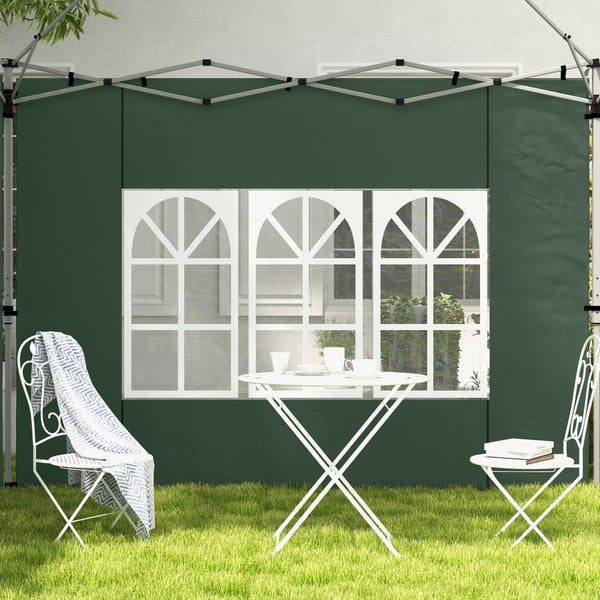 Grüne Pavillon-Seitenwand mit drei Bogenfenstern, davor ein weißer Bistrotisch und zwei Metallstühle auf einer Rasenfläche.