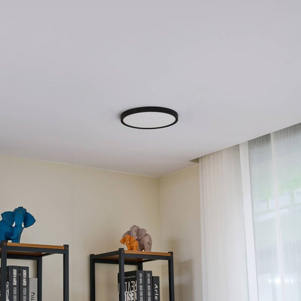 Rundes schwarzes LED-Deckenpaneel montiert an der Decke in einem modern eingerichteten Zimmer mit Regalen.