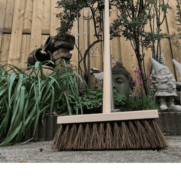 Kehrbesen mit Holzstiel vor Gartendekoration