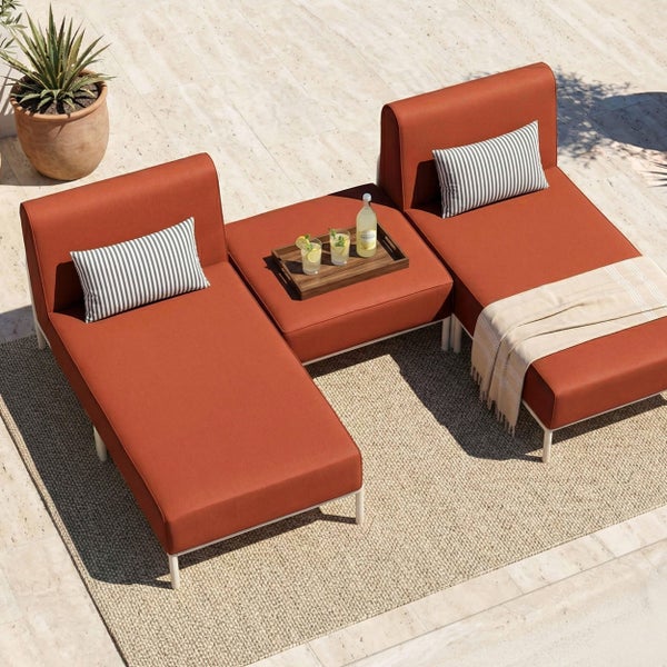 Modulares Garten-Lounge-Set mit gepolsterten Sonnenliegen und einem Mittelelement auf einer Steinterrasse mit Außenteppich.