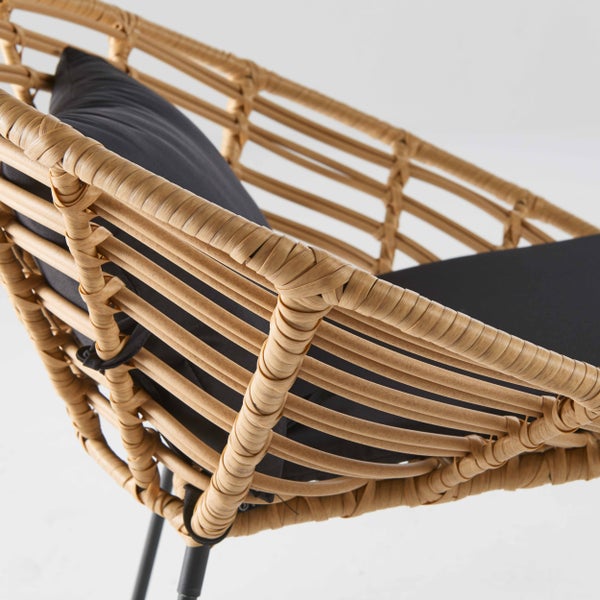 Detailansicht eines Gartenstuhls aus Polyrattan-Geflecht mit einem dunklen Sitzkissen.