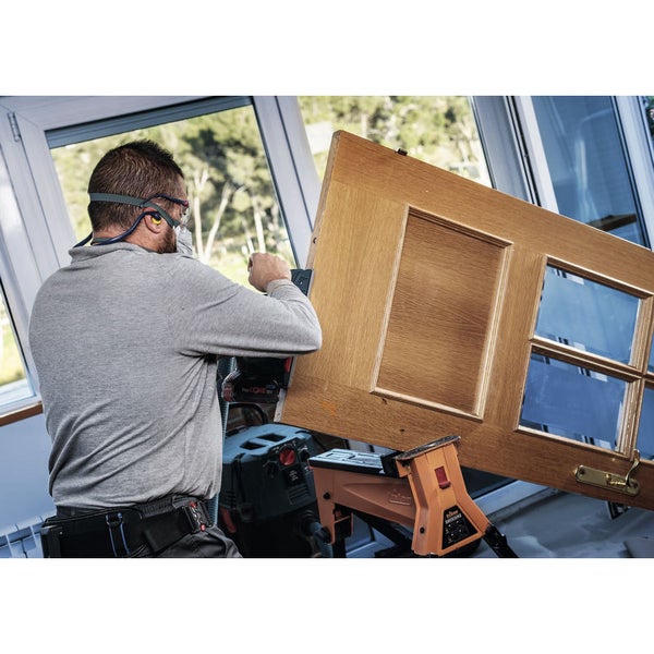 Ein Mann hobelt eine Holztür mit einem Elektrohobel.