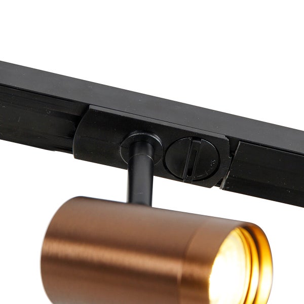 Zylindrischer Strahler in Bronzeoptik an einer schwarzen Schiene für ein Schienensystem.