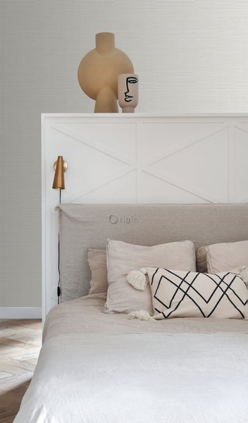 Schlafzimmer mit Bett, Kissen, Dekorationsgegenständen und Wandleuchte