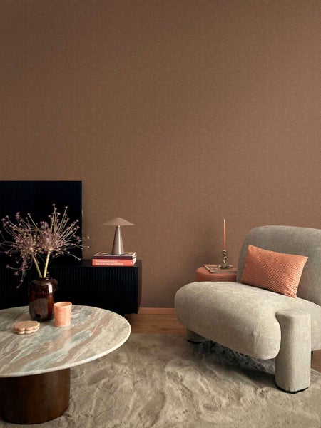 Wohnzimmer mit brauner Vliestapete, modernem Sessel, Marmortisch und Dekorationsgegenständen in einer eleganten und gemütlichen Wohnumgebung.