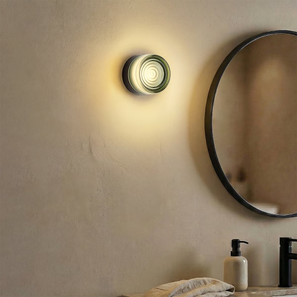 Moderne runde Wandleuchte mit geriffeltem Glas in einem Badezimmer neben einem runden Spiegel und einem Waschbecken mit Armatur.