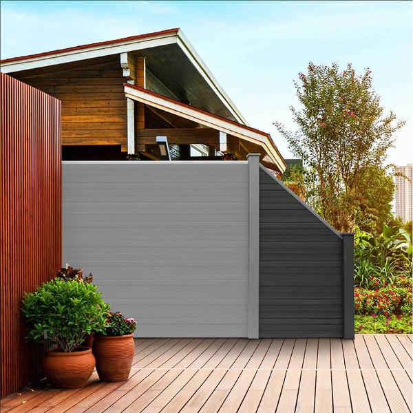 Moderne Sichtschutzwand aus WPC Elementen auf einer Holzterrasse im Garten vor einem Wohnhaus.