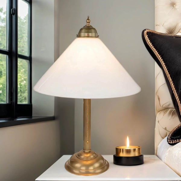 Tischleuchte mit Kegelform und Kerze auf einem Nachttisch.