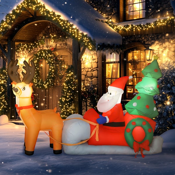 Aufblasbare Weihnachtsdekoration mit Weihnachtsmann im Schlitten und Rentier vor einem beleuchteten Haus im Schnee.