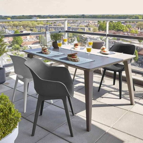 Modernes Gartenmöbel-Set auf einem hellen Balkon mit einem rechteckigen Tisch und vier Schalensitz-Stühlen, eingedeckt für eine Mahlzeit.