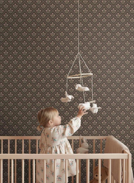 Vliestapete mit floralem Muster in einem Kinderzimmer mit Gitterbett aus Holz und Kleinkind, das nach einem Mobile greift.