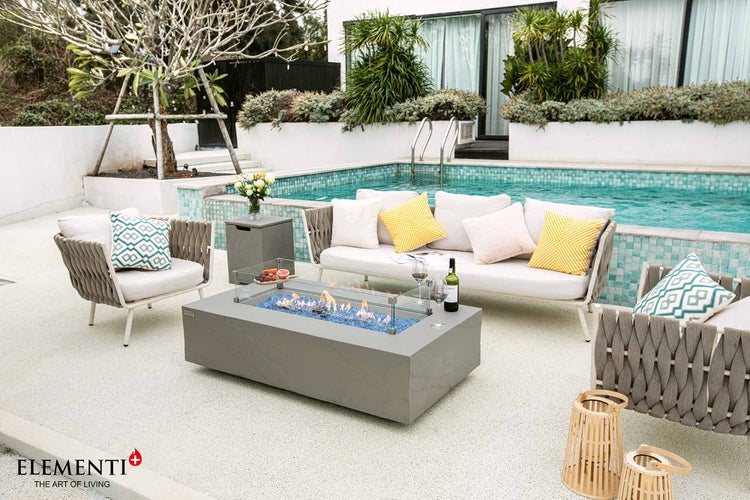 Moderne Gartenlounge am Pool mit rechteckigem Gasfeuertisch, Sofa, Sesseln mit Seilgeflecht, dekorativen Kissen und Elementi Logo.