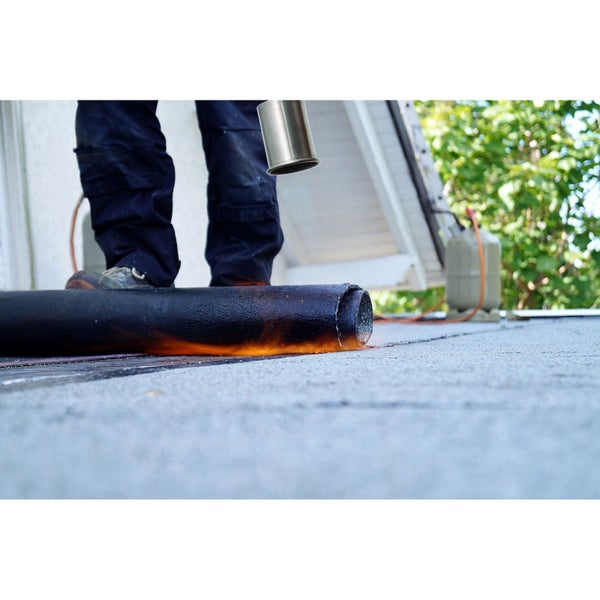 Eine Person verlegt Bitumenschweißbahnen auf einem Flachdach mithilfe eines Gasbrenners.