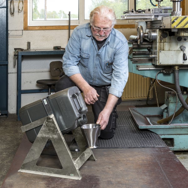 Eine Person gießt Flüssigkeit aus einem Kanister in einen Messbecher in einer Werkstatt.