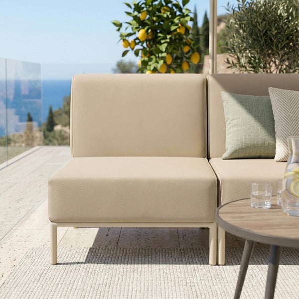 Modulares Gartensofa-Element auf einer hellen Terrasse mit Meerblick, Zitronenbaum und Teppich.