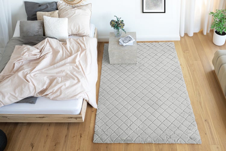 Rechteckiger Teppich mit Rautenmuster vor einem Bett in einem modern eingerichteten Schlafzimmer mit Holzboden