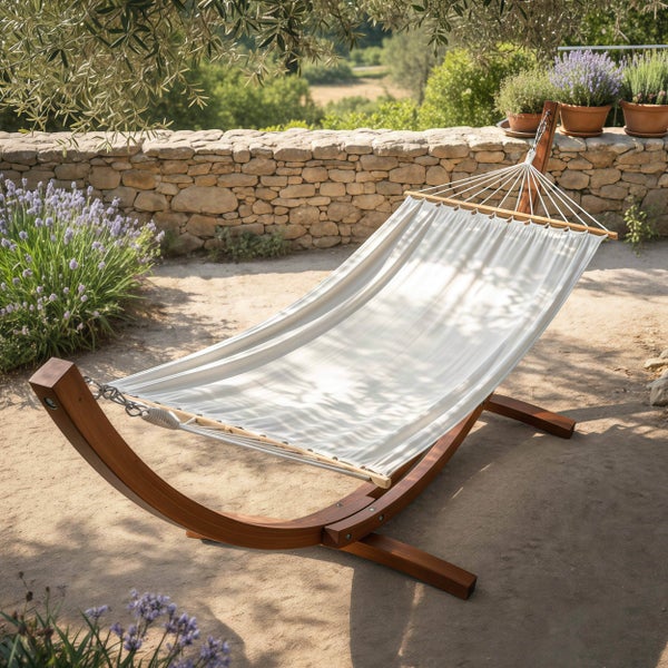 Hängematte mit gebogenem Holzgestell in einem hellen Garten vor einer Steinmauer mit Lavendelpflanzen.