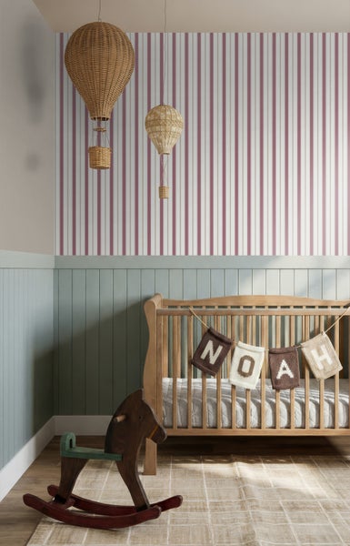 Kinderzimmer mit gestreifter Tapete, grüner Holzvertäfelung, hölzernem Babybett mit Namensbanner, Schaukelpferd, Heißluftballons und hellem Teppich.