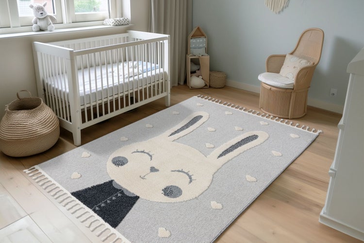 Ein Kinderteppich mit Hasenmotiv liegt in einem hellen, freundlichen Kinderzimmer mit Kinderbett, Korbstuhl und Holzfußboden.