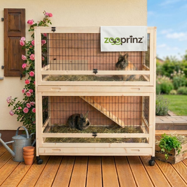 Heller Außenbereich mit zweistöckigem Kleintierstall aus Holz auf einer Terrasse. Mit Rampe, Rollen und zooprinz Logo.