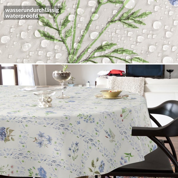 Rundes, wasserundurchlässiges Tischtuch mit blauem Blumenmuster in einem hellen Wohnzimmer. Nahaufnahme zeigt abperlende Wassertropfen.