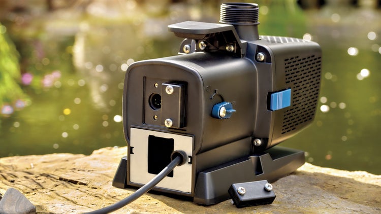 Schwarze Teichpumpe mit Anschlussbuchse, Drehregler und Stromkabel auf einem Stein an einem Gartenteich.