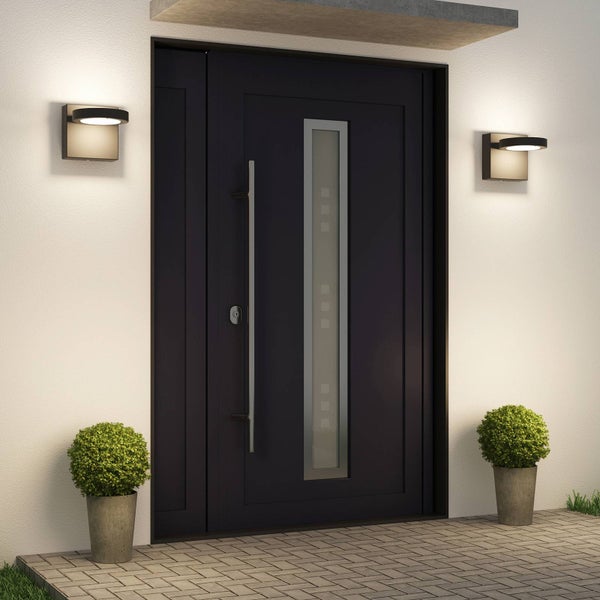 Moderne dunkle Haustür mit schmalem Glasausschnitt, langem Edelstahlgriff und zwei beleuchteten Außenwandleuchten im Eingangsbereich.