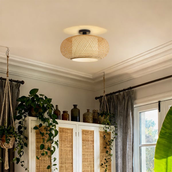 Deckenleuchte aus geflochtenem Bambus in einem hellen Wohnraum mit Zimmerpflanzen und Schrank im Boho-Stil.