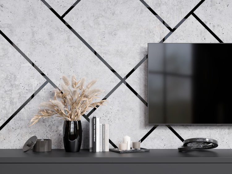 Dekoratives Wohnzimmer mit Fernseher, Zierpflanzen und Dekorationsgegenständen auf einem Regal vor einer Betonwand mit geometrischen Formen.