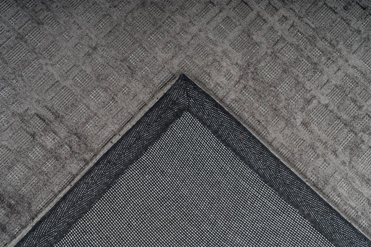 Nahaufnahme einer grauen Teppichecke mit strukturierter Oberfläche, Gittermuster und rutschhemmender Rückseite.